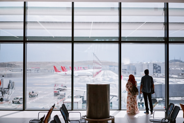 A couple stands looking out the window of their terminal
